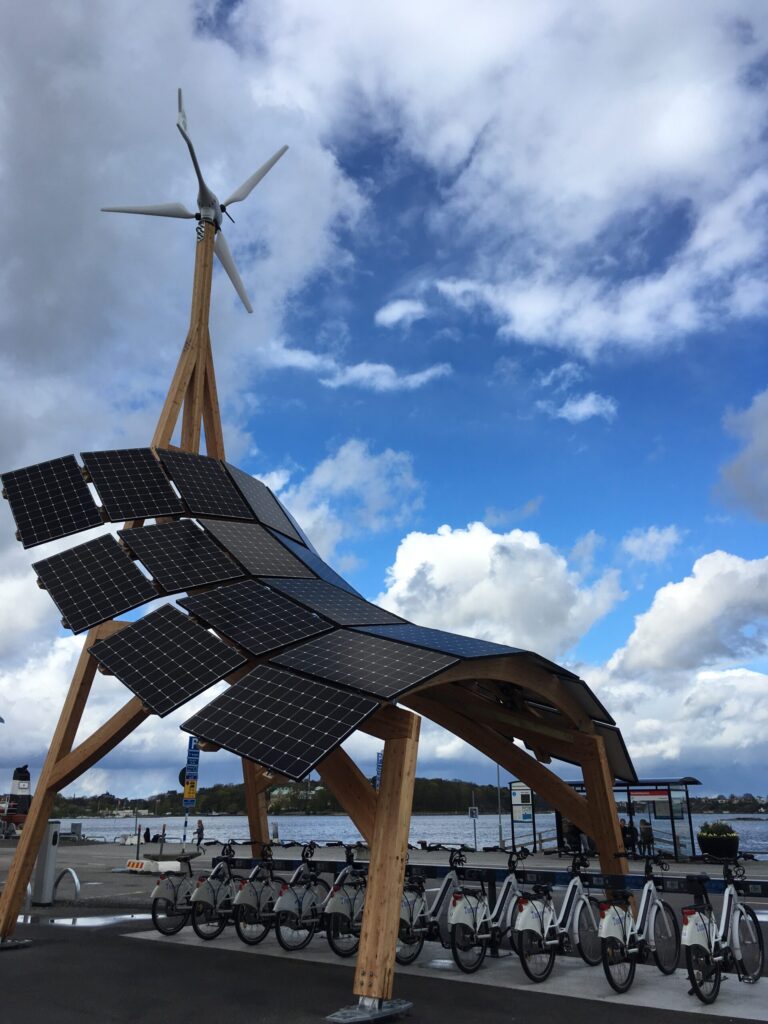 Bilden visar ett cykelställ för elcyklar som får el via solceller och ett litet vinkraftverk.